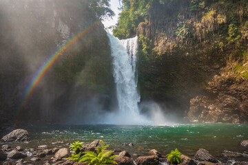 Majestic waterfall cascading into crystal-clear pool with mist and rainbow glow, cinematic nature landscape