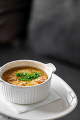 Hot French onion soup in a white ceramic ramekin, topped with melted cheese and parsley, served on a plate with napkin. Cozy comfort food in a rustic indoor setting
