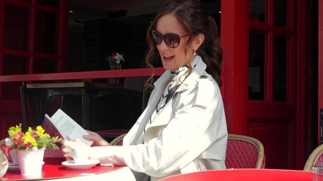Smiling woman enjoying coffee and reading at red Parisian cafe terrace 
