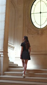 Elegant woman on grand staircase in Louvre Museum Paris with natural light 