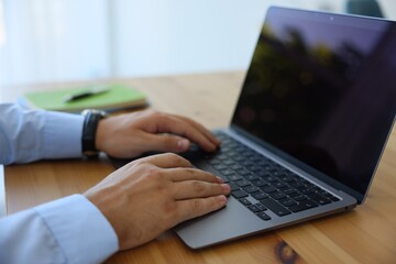 Man working on laptop at wooden table indoors, closeup
