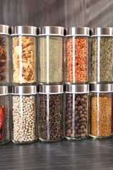 Different spices in glass jars on grey wooden table, closeup