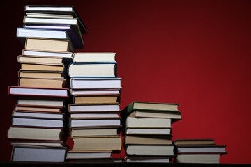 Many stacked books on table against red background. Space for text