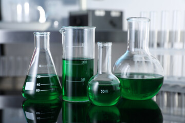 Different glassware with green liquid on table in laboratory, closeup
