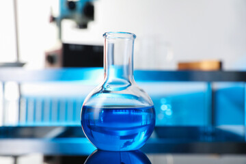 Glass flask with blue liquid on table in laboratory, closeup