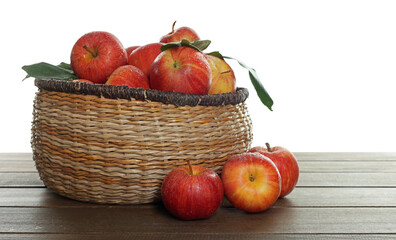 Fresh apples in wicker basket and green leaves on wooden table against white background
