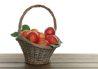 Fresh apples in wicker basket and green leaves on wooden table against white background