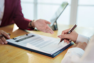 Smiling businesswoman holding calculator while discussing real estate financial planning with client, showing house model and documents on office desk.