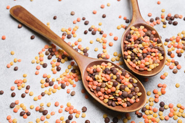 Colorful lentils in wooden spoons scattered on a textured surface, showcasing a variety of hues and sizes, emphasizing healthy cooking and vibrant ingredients