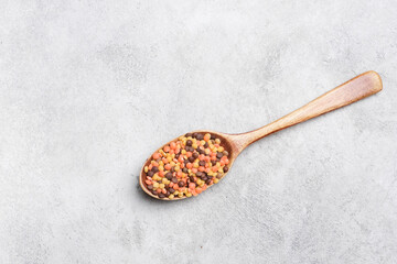 Wooden spoon filled with colorful lentils seeds resting on a textured gray surface, showcasing vibrant colors and natural materials in culinary context