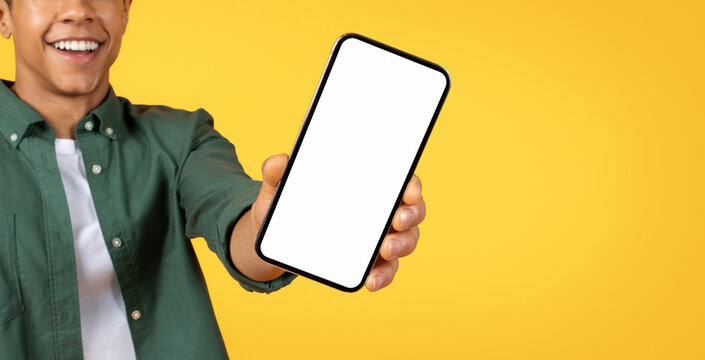 Cropped of african american man in casual clothes extends a smartphone towards the camera, the screen blank and ready for content