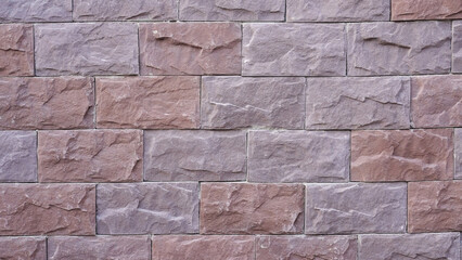 Finished section of a facade with decorative stone tiles installed on the wall. Close-up view of completed masonry work after exterior renovation.