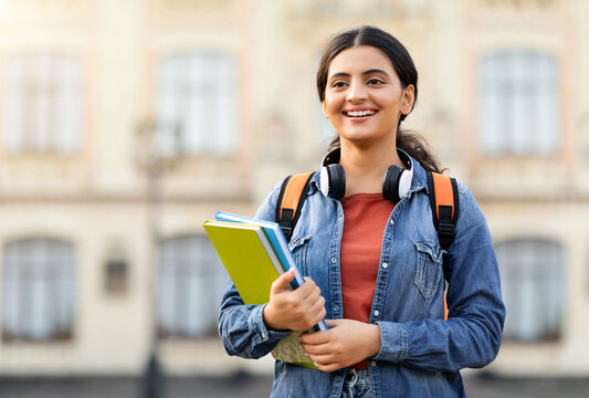 Fototapeta Portrait of glad hindu lady student in casual with books posing outdoors and smiling at camera, ready for lesson in university campus, free space. Study, knowledge at college