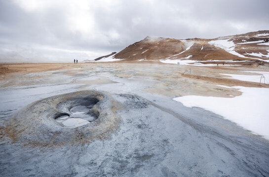 bubbling mud pots with snow covered mountains at Hverir geothermal area, North Iceland - Powered by Adobe