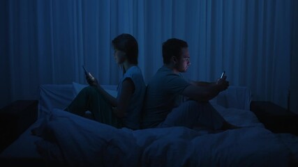 A couple sits back to back in bed at night using smartphones - Powered by Adobe