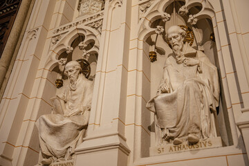 The image captures detailed marble sculptures of Saint Athanasius and Saint Gregory of Nazianzus in an ornate church wall niche. The figures are seated with halos and books, surrounded by Gothic