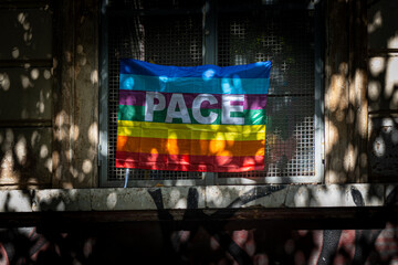 Peace flag with the italian word PACE on a window with dappled light. Rainbow flag as a symbol of hope, anti-war protest and activism in a gritty urban context.
