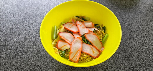 Top view bowl of noodles. Noodles with roasted red pork and boiled dumplings served in green bowl.  Noodles without soup garnished with sliced ​​roast pork, shrimp dumplings, Chinese kale,fried garlic