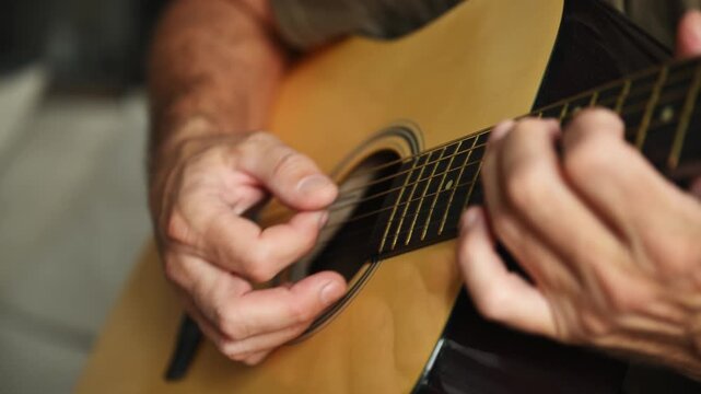 Casual older musician learning to play acoustic guitar in living room, home practice concept. 4K.