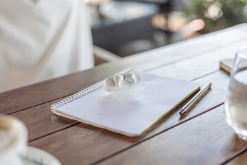 A blank notebook and a pen on a wooden table. A glass of water is nearby. The scene suggests a remote work or study environment.