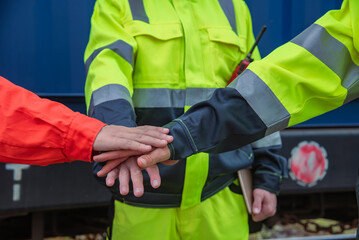Teamwork and collaboration are essential in safety focused environments, as shown by hands of workers in bright safety gear coming together in unity