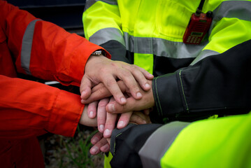 Teamwork and collaboration are essential in safety focused environments, as shown by hands of workers in bright safety gear coming together in unity