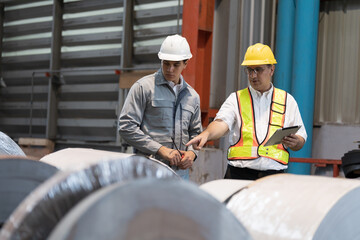 Metalwork manufacturing, coil, storage of rolls metal sheet, warehouse of raw materials. Group of male factory worker inspecting quality of rolls metal sheet in factory, wearing safety uniform