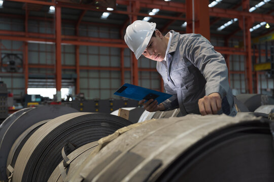 Metalwork manufacturing, warehouse of raw materials. Male factory worker inspecting quality rolls of metal sheet in factory during manufacturing process, wearing safety uniform