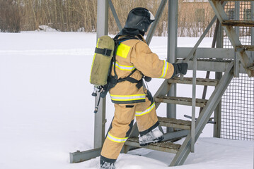 A firefighter in a helmet and protective clothing, with a breathing apparatus, climbs the stairs. In winter, firefighters conduct outdoor training. The rescue service.