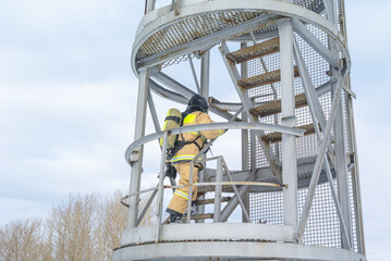 A firefighter in a helmet and protective clothing, with a breathing apparatus, climbs the stairs. In winter, firefighters conduct outdoor training. The rescue service.