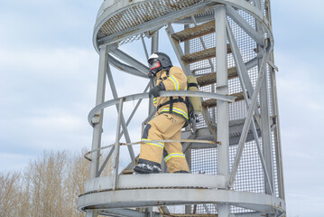 A firefighter in a helmet and protective clothing, with a breathing apparatus, climbs the stairs. In winter, firefighters conduct outdoor training. The rescue service.