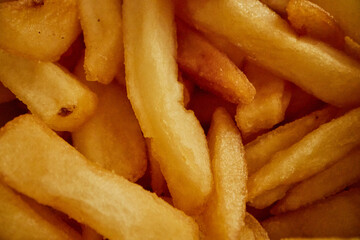 Close up showing golden French fries stacked together, crispy texture visible on surface, no people present, emphasizing detail of cooked potato snack, background fully filled with fries