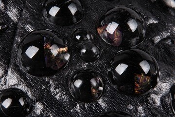Bubbles of black liquid on textured, metallic grey background