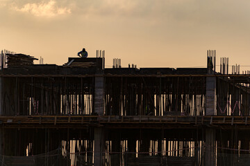 A silhouette of a construction site with a worker on the roof against a cloudy sky at sunset. The image captures the hard work and progress of building, symbolizing industry and development.