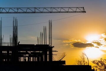 Silhouette of a construction site with a crane against a dramatic sunset sky. The scene conveys a sense of progress, hard work, and the end of a workday.
