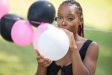 Naklejka premium Beautiful young woman blowing white balloon during joyful park summer celebration