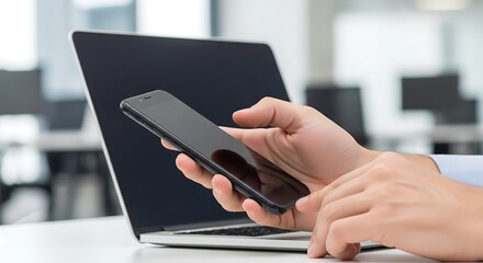 Fototapeta premium Person Using Smartphone in Modern Office Workspace with Laptop and Natural Light