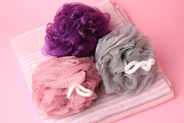 Colorful shower puffs and towel on pink background, above view