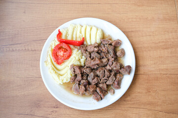 Traditional beef dish served with mashed potatoes, tomato, and red pepper. Homemade comfort meal on a wooden table.