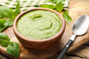 Tasty green pesto in bowl and basil leaves on wooden table, closeup