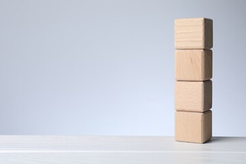 Blank cubes on white wooden table against light grey background, space for text