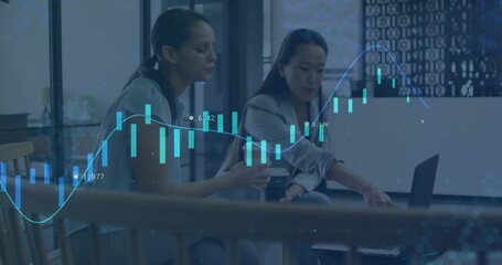 Collaborating women reviewing financial chart overlay in office lounge, with laptop, coffee cup