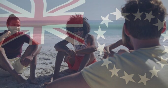 Chatting friends wearing T-shirts and shorts sitting on beach, with Union Jack and stars overlay