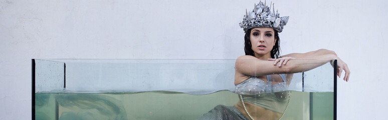 Young woman in shimmering attire gracefully poses in a stunning glass tank filled with water