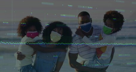 Embracing family wearing colorful face coverings standing on sandy beach at dusk, ocean backdrop
