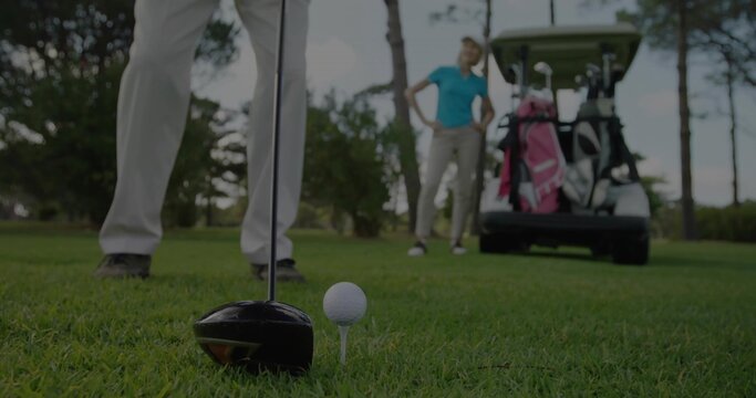 Positioning driver club head behind golf ball on tee at tee box, with golf cart, bags