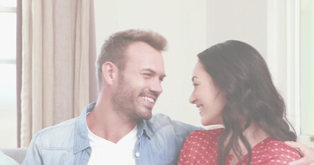 Smiling couple in casual clothing chatting on sofa at home, with beige curtains and pillows