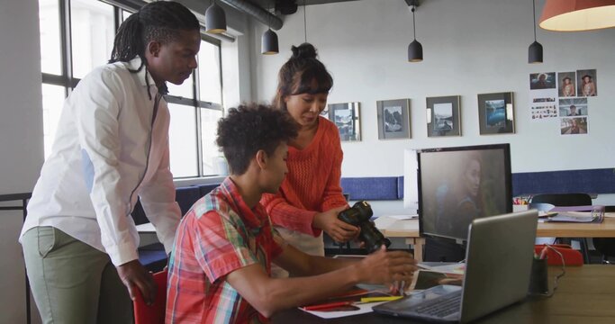 Collaborating colleagues exchanging DSLR camera and reviewing printed layouts at creative workspace - Powered by Adobe