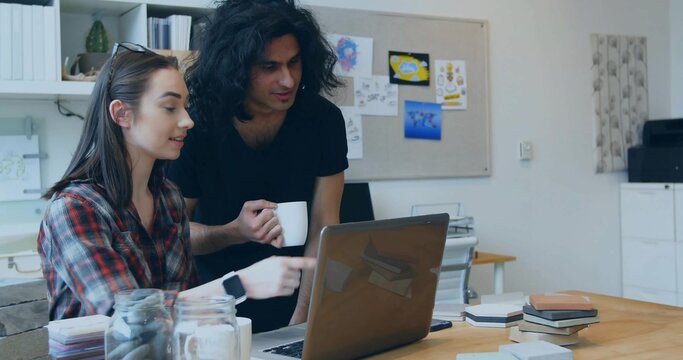 Collaborating team focusing on laptop screen at design studio desk, with coffee mug and sketches - Powered by Adobe