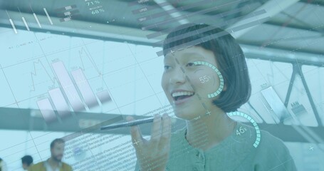 Speaking woman in green top holding smartphone in modern office, with data overlays and blurred men